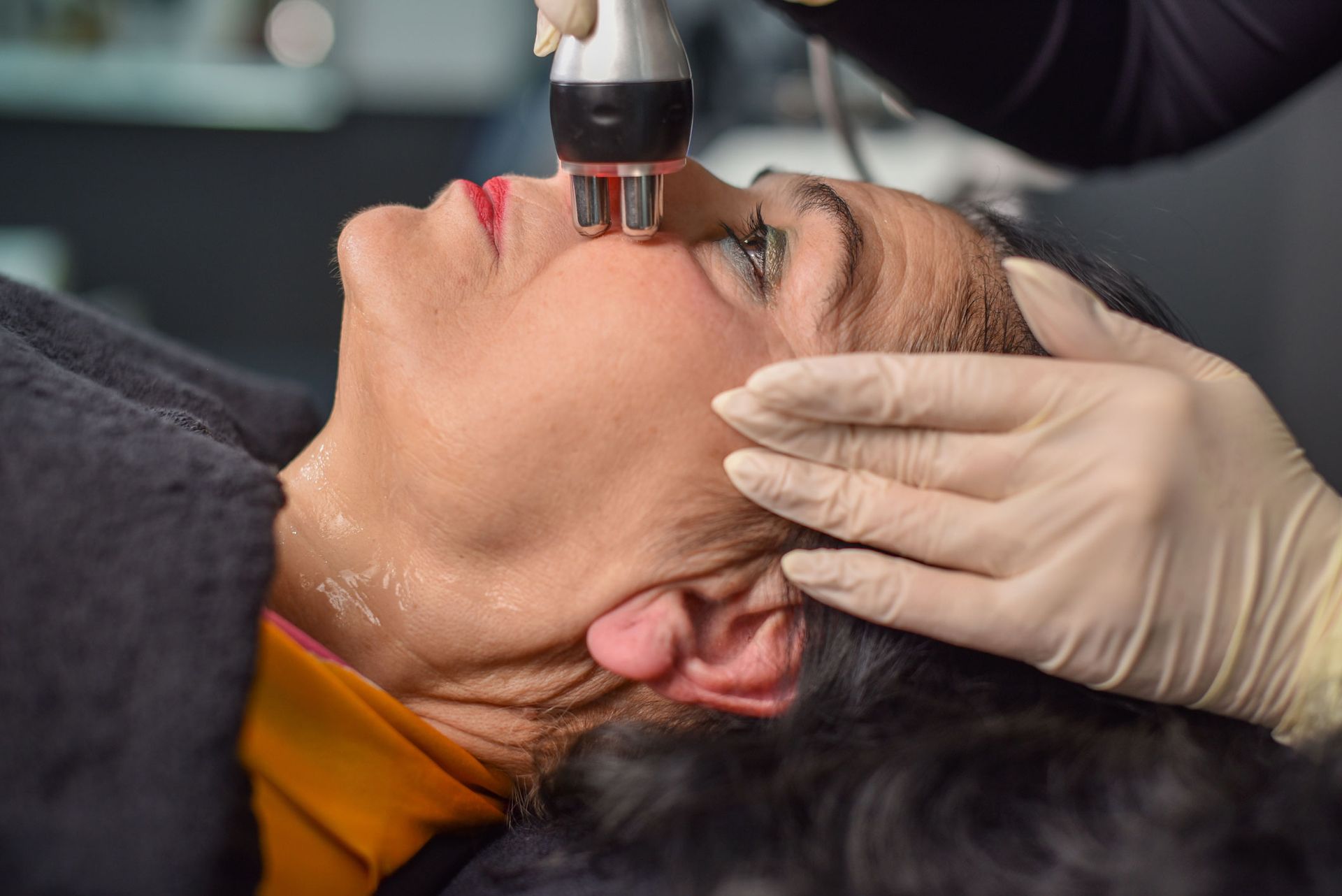 Woman receiving facial treatment with a handheld device, in a spa setting.