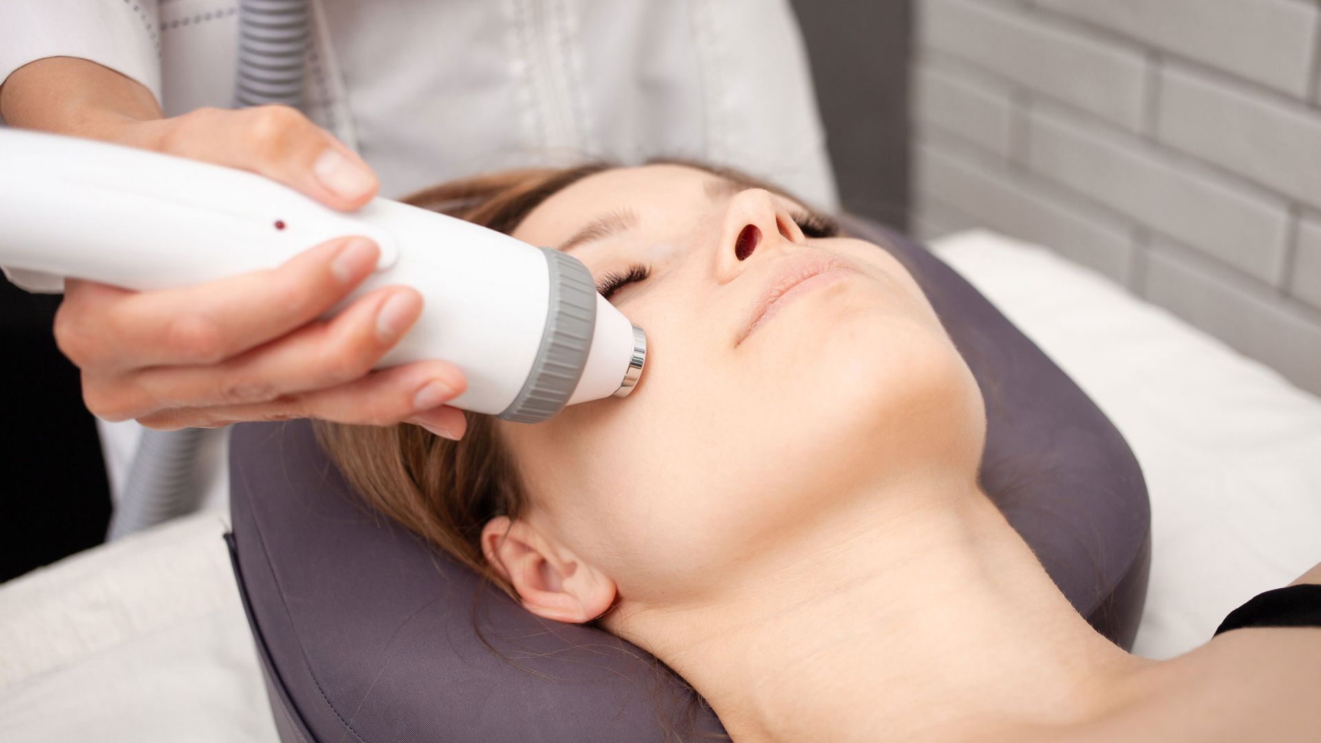 A person receiving facial skin treatment with a handheld device, indoors.