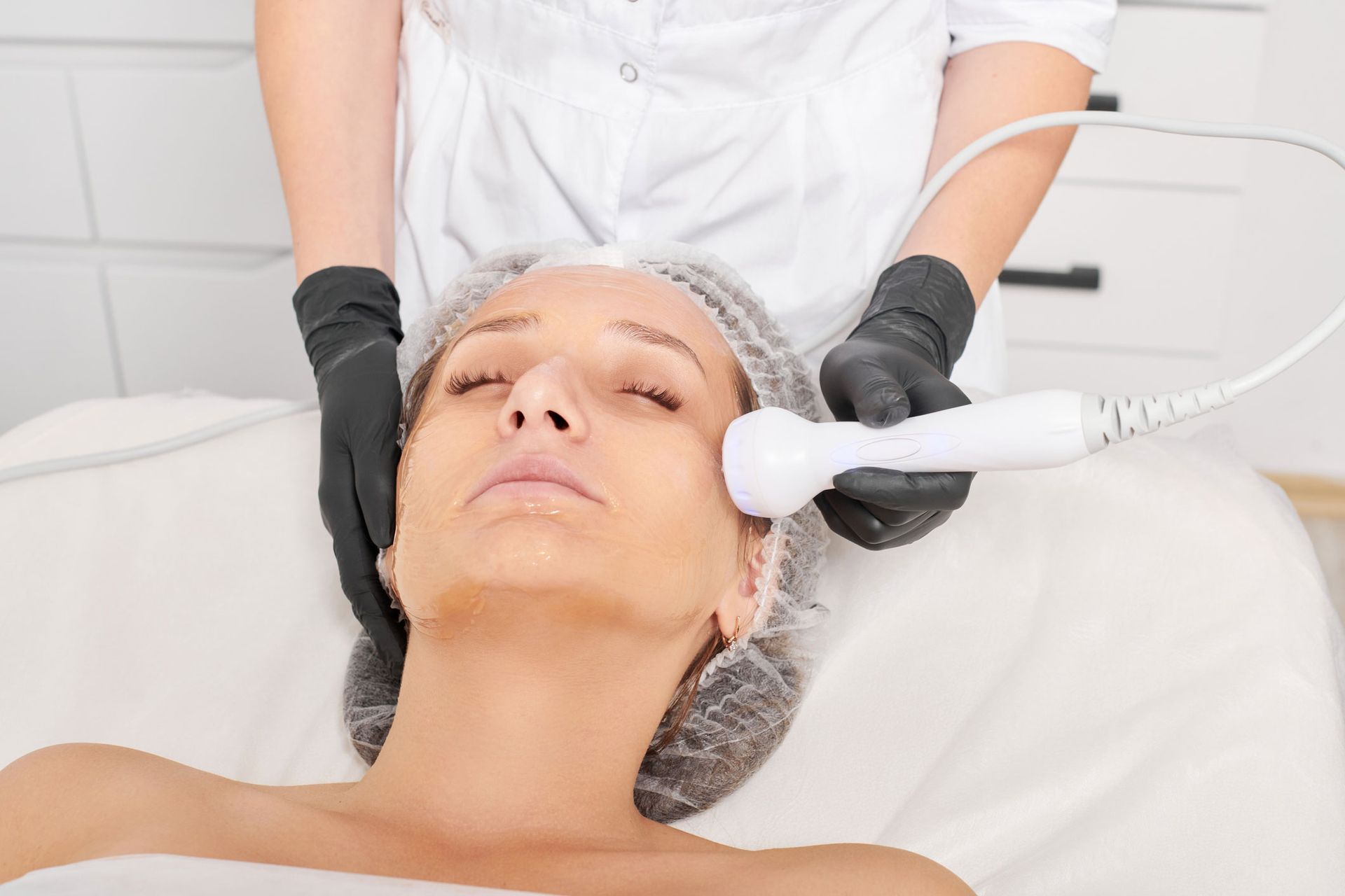 Woman receiving facial treatment in a spa, using a handheld device.