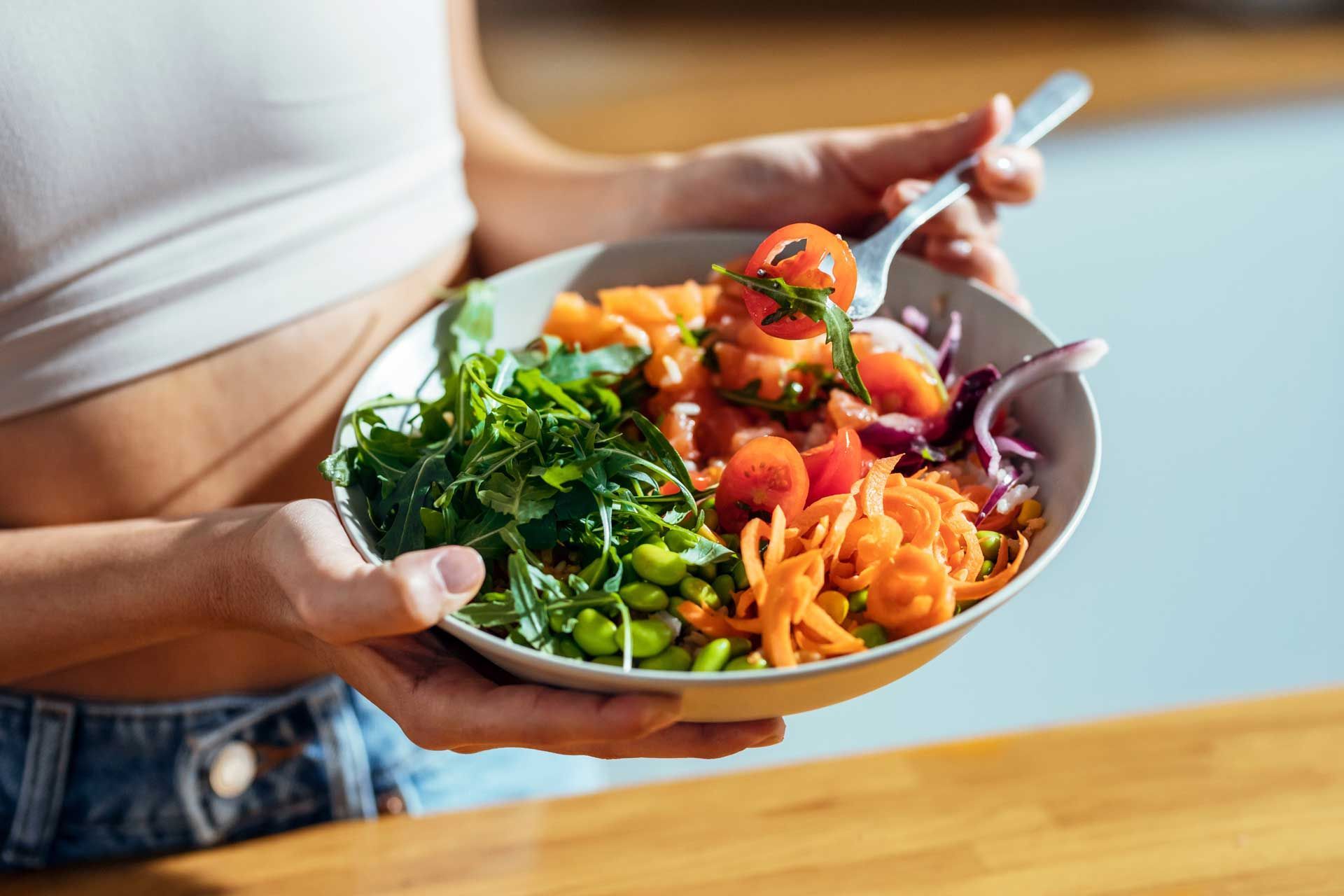 Person holding a bowl of colorful salad with a fork.