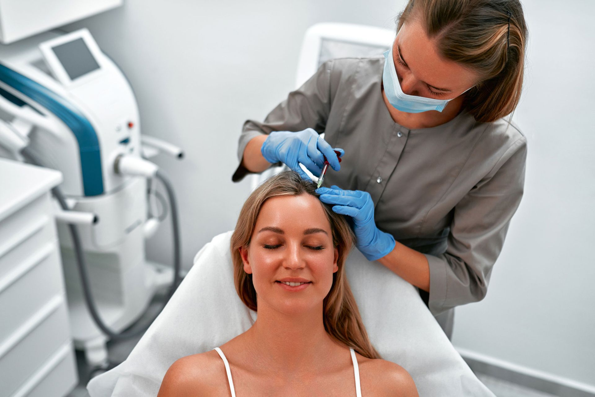 Woman receiving scalp injections in a medical setting. A clinician wearing gloves and a mask is administering the injections. Woman receiving scalp injections in a medical setting. A clinician wearing gloves and a mask is administering the injections.