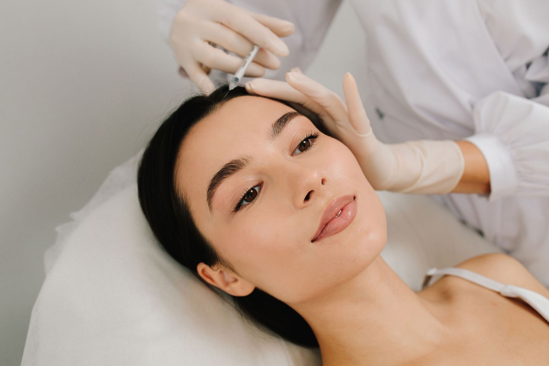 Person receiving an injection on their forehead, lying down. Healthcare worker in gloves. Person receiving an injection on their forehead, lying down. Healthcare worker in gloves.