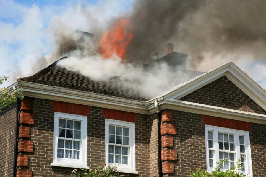 Heavy smoke and flames rising from the roof and attic of a brick home with white trim windows