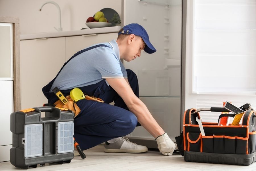 Buckled laminate flooring in front of a refrigerator with a visible water trail leading from behind the appliance toward the kitchen island