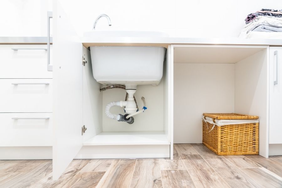 Open under-sink kitchen cabinet showing water staining on the cabinet floor and swollen particleboard near the drain connection