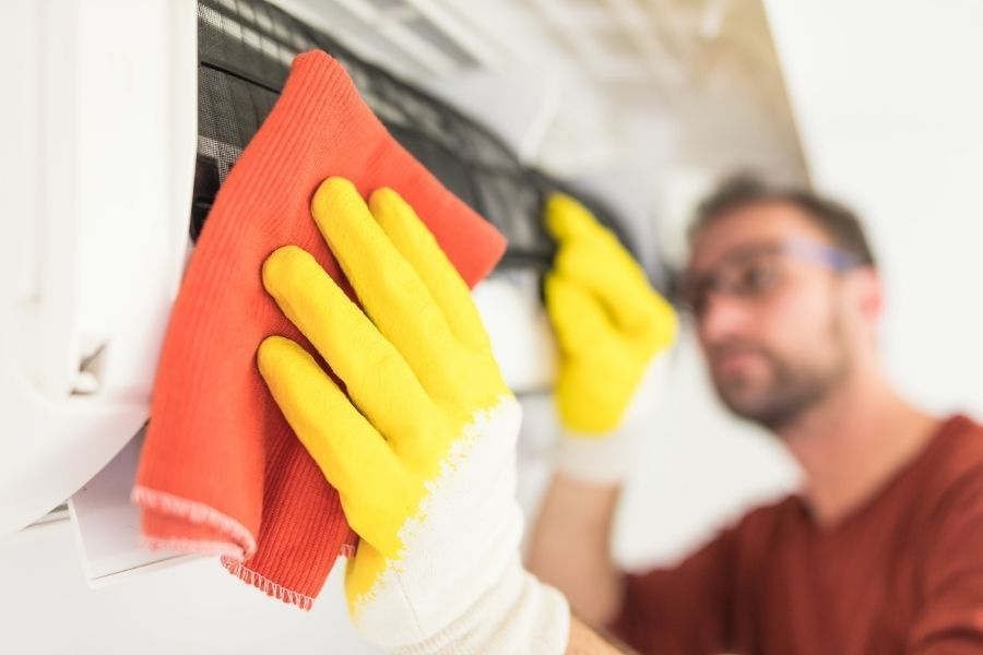 Homeowner wiping down an AC unit with a cloth for routine maintenance