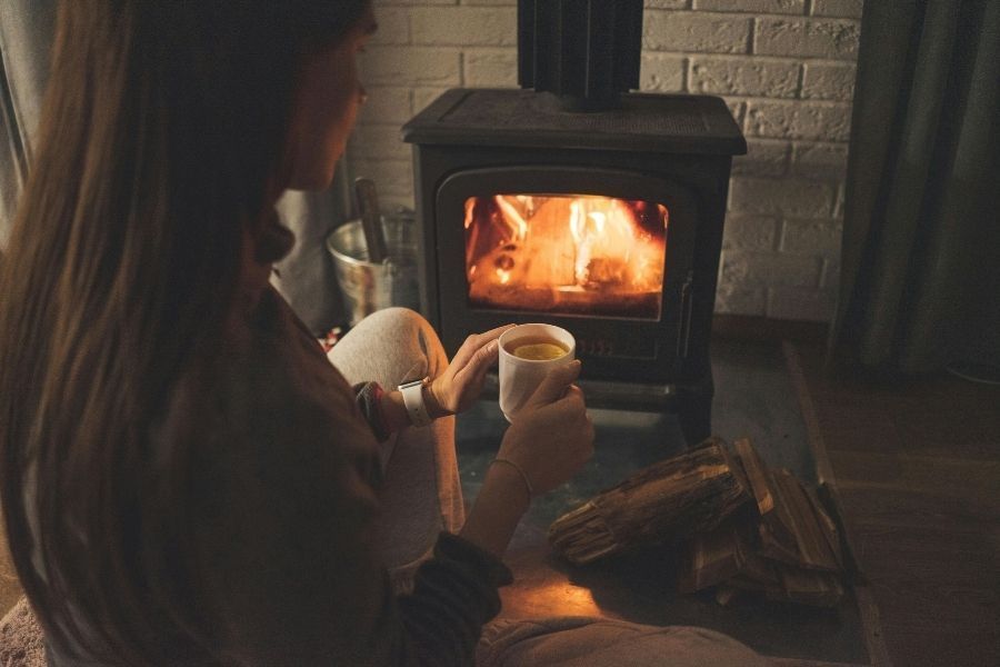 Woman relaxing by wood stove with hot drink