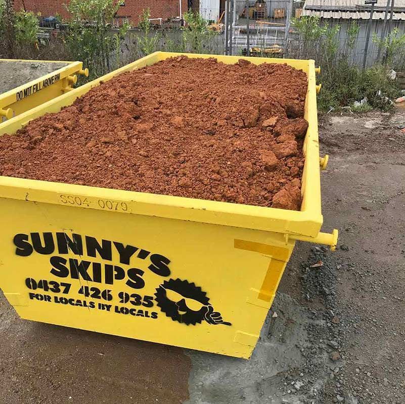 A Yellow Skip Bin Filled With Dirt Is Sitting On The Ground — Sunny's Skips in Port Macquarie, NSW