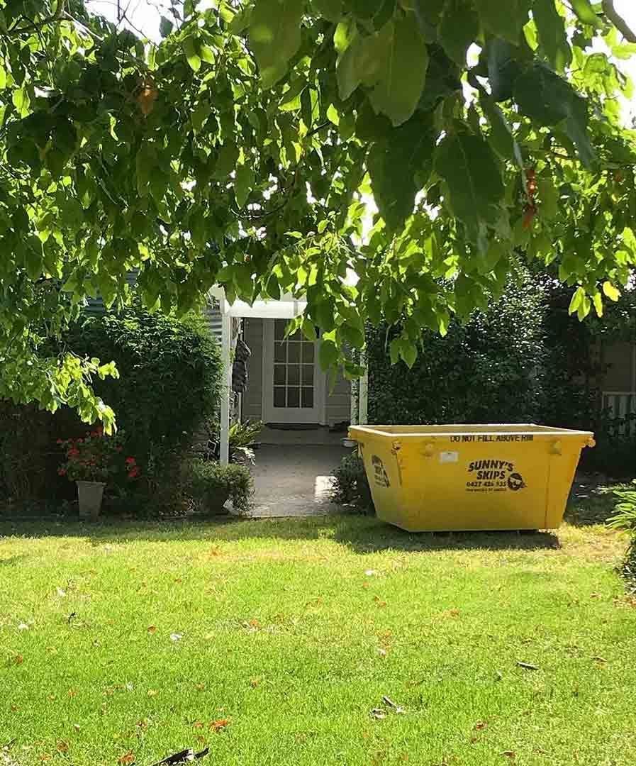 A Yellow Skip Bin Is Sitting In The Grass In Front Of A House — Sunny's Skips in Port Macquarie, NSW