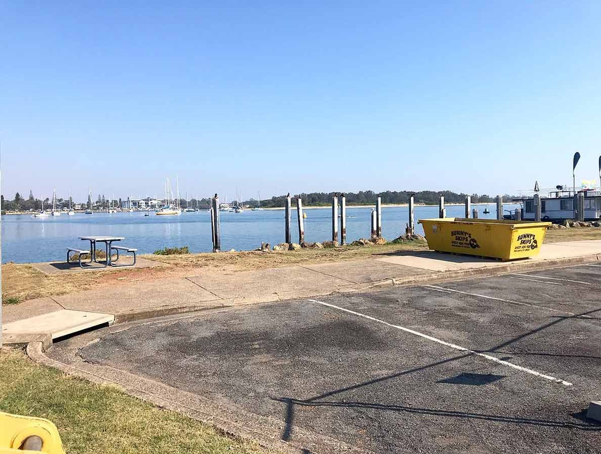 A Yellow Skip Bin Is Parked In A Parking Lot Next To A Body Of Water — Sunny's Skips in Port Macquarie, NSW