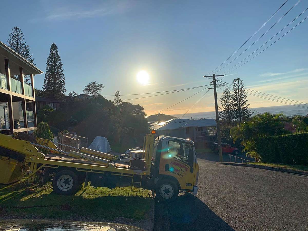A Yellow Tow Truck Is Parked On The Side Of The Road In Front Of A House — Sunny's Skips in Wauchope, NSW