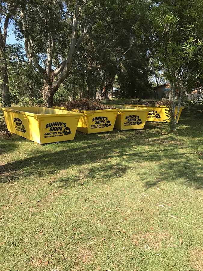 A Row Of Yellow Skip Bins Sitting On Top Of A Lush Green Field — Sunny's Skips in Port Macquarie, NSW