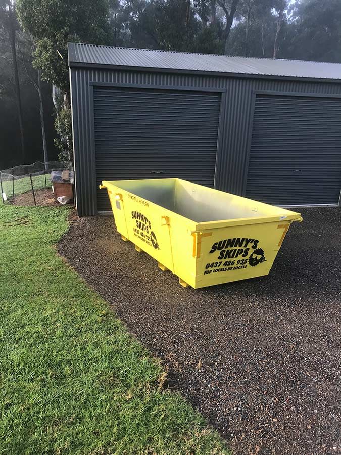 A Yellow Skip Bin Is Sitting In Front Of A Garage — Sunny's Skips in Port Macquarie, NSW