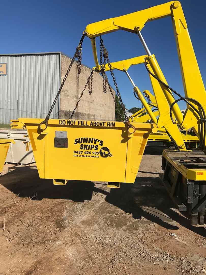 A Yellow Skip Bin Is Being Lifted By A Crane — Sunny's Skips in Port Macquarie, NSW