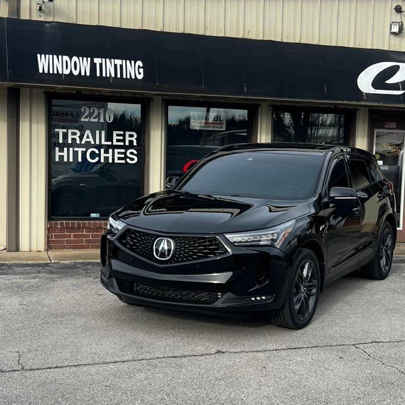 Black Acura SUV parked in front of a window tinting and trailer hitch business. The windows are tinted.