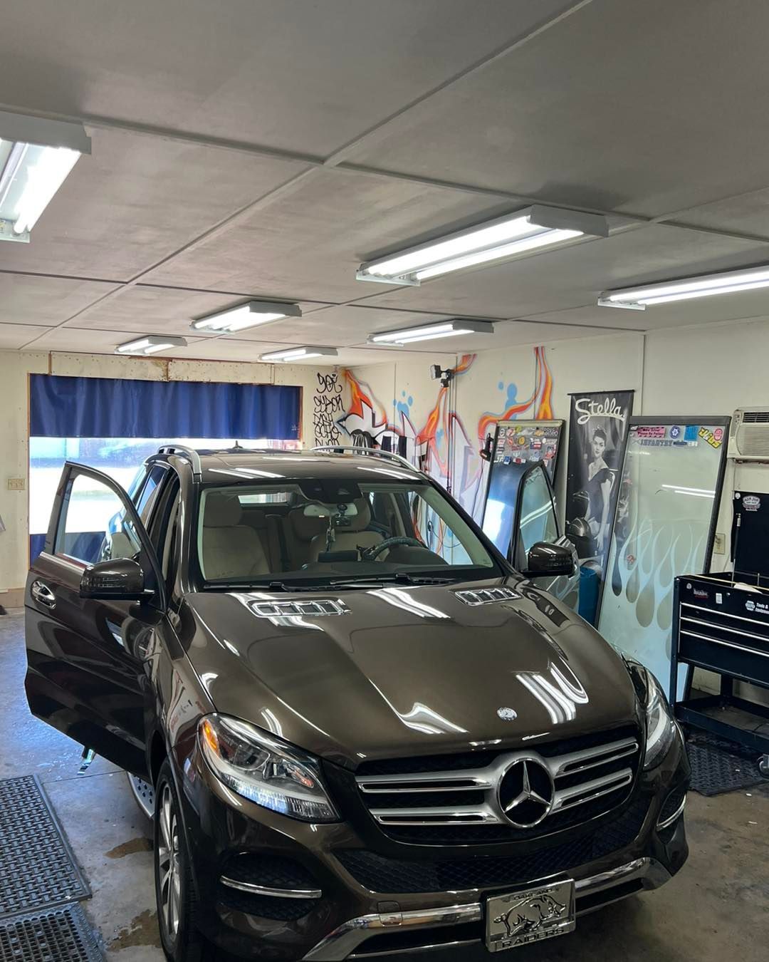 Brown Mercedes SUV with open door in a garage, window tinting equipment visible.