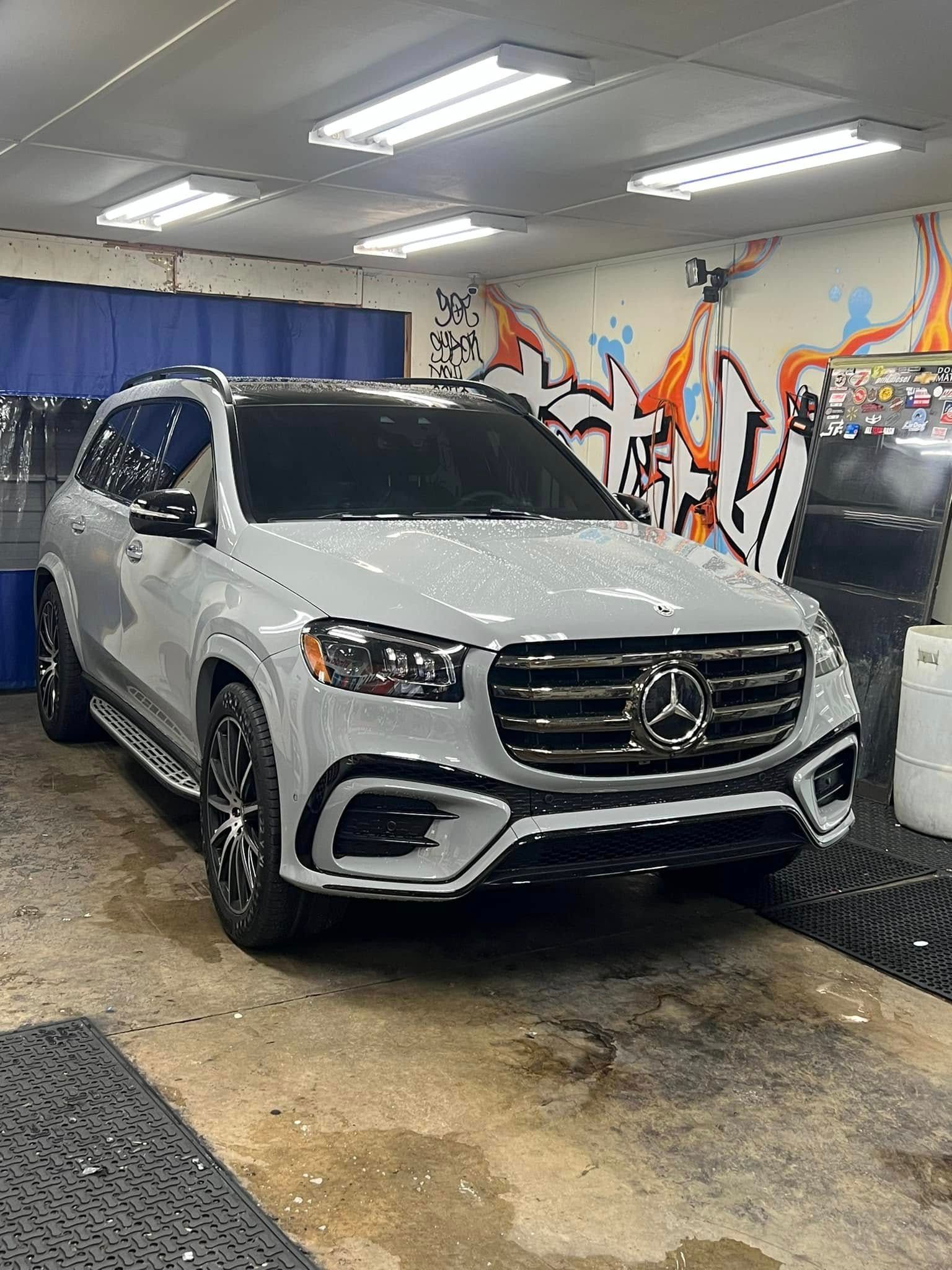 Light gray Mercedes-Benz GLS SUV parked in a car wash bay, with black accents and wheels.