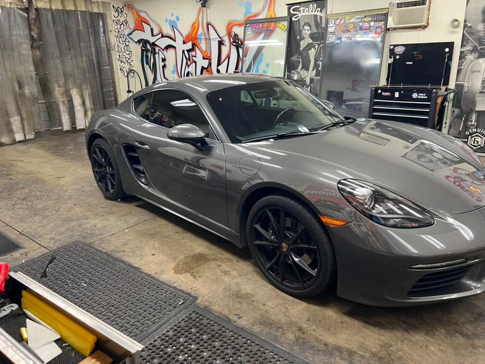 Gray Porsche Cayman sports car in a garage with graffiti and tools.