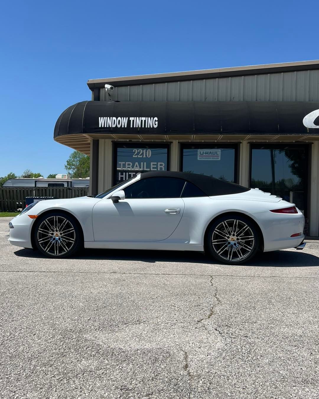 White Porsche convertible parked outside a window tinting business on a sunny day.