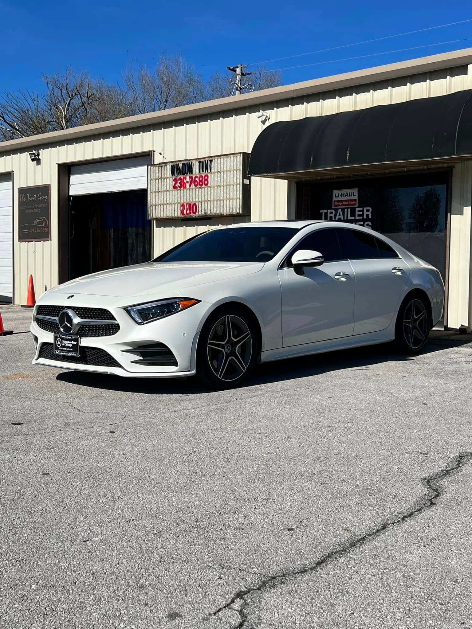 White Mercedes car parked outside a building with a black awning on a sunny day.