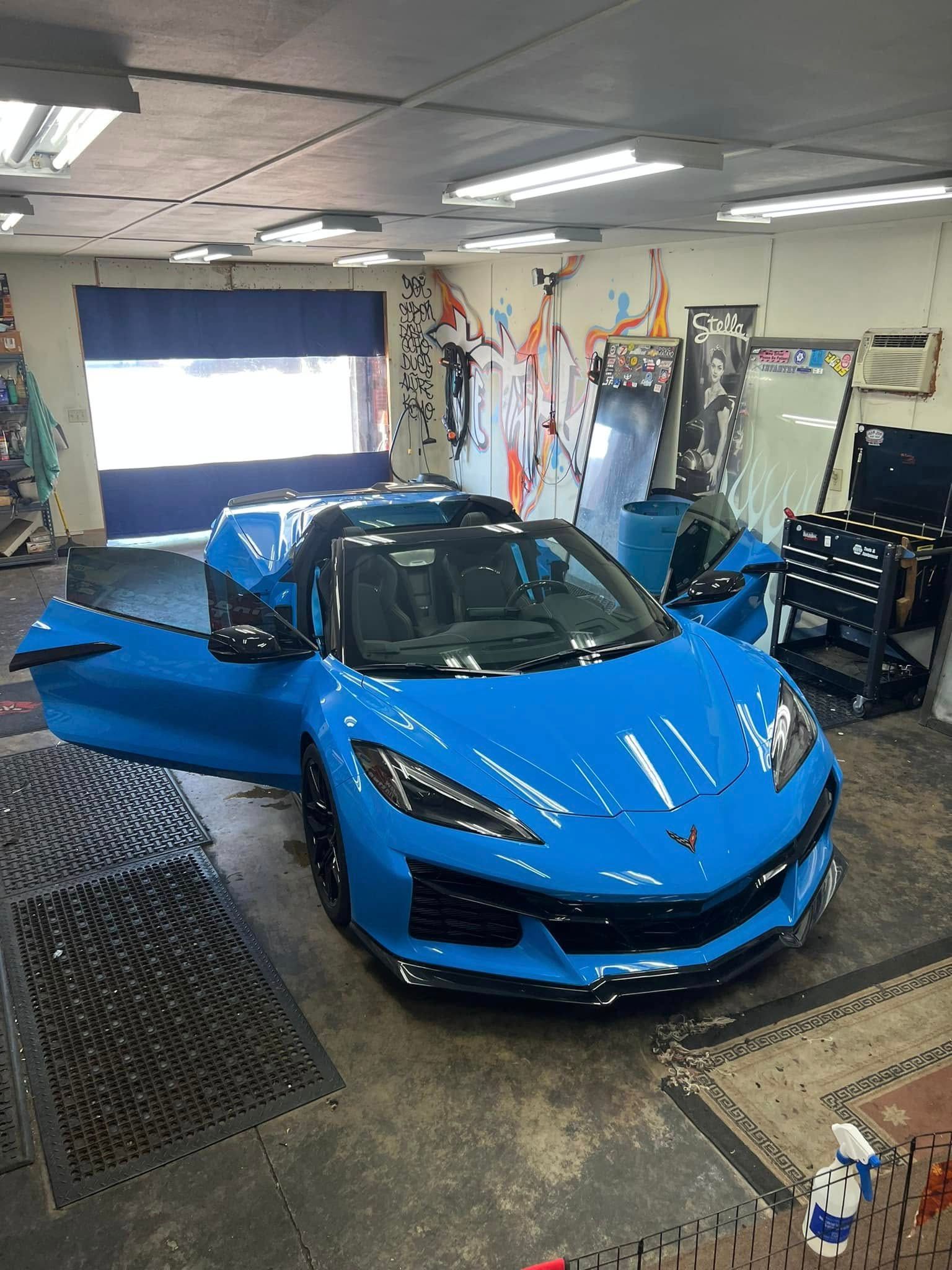 White sports car with black racing stripes on a rotating platform in a showroom.