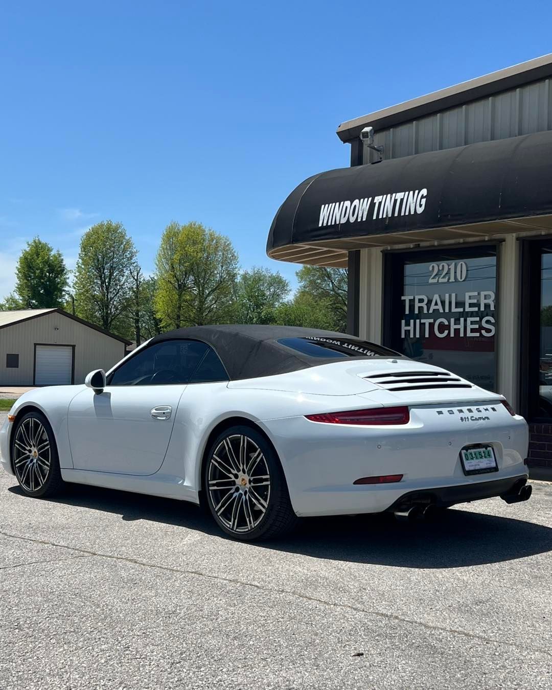 White Porsche convertible parked outside a window tinting business on a sunny day.