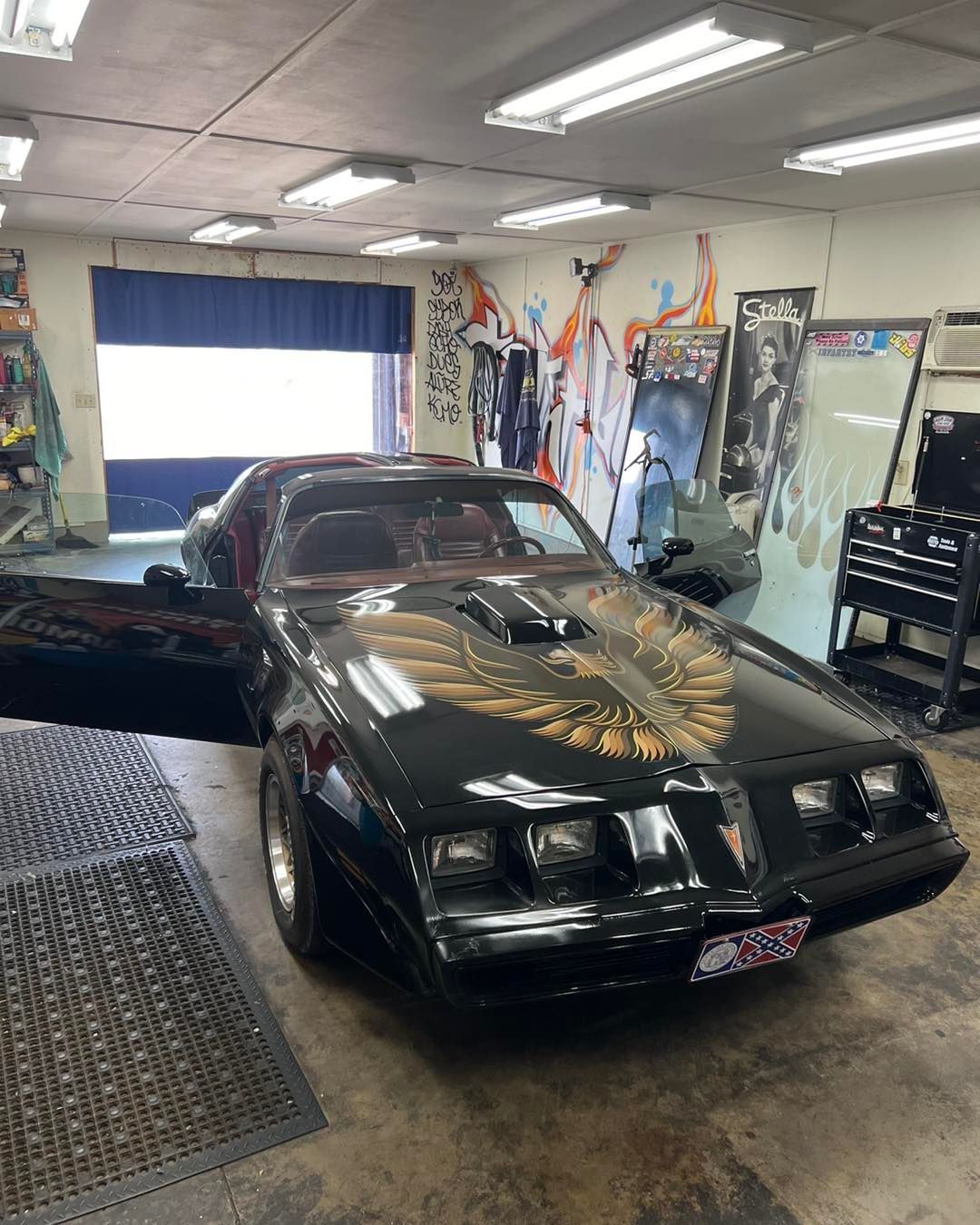 Black Pontiac Trans Am with gold bird emblem, door open, parked in a garage.