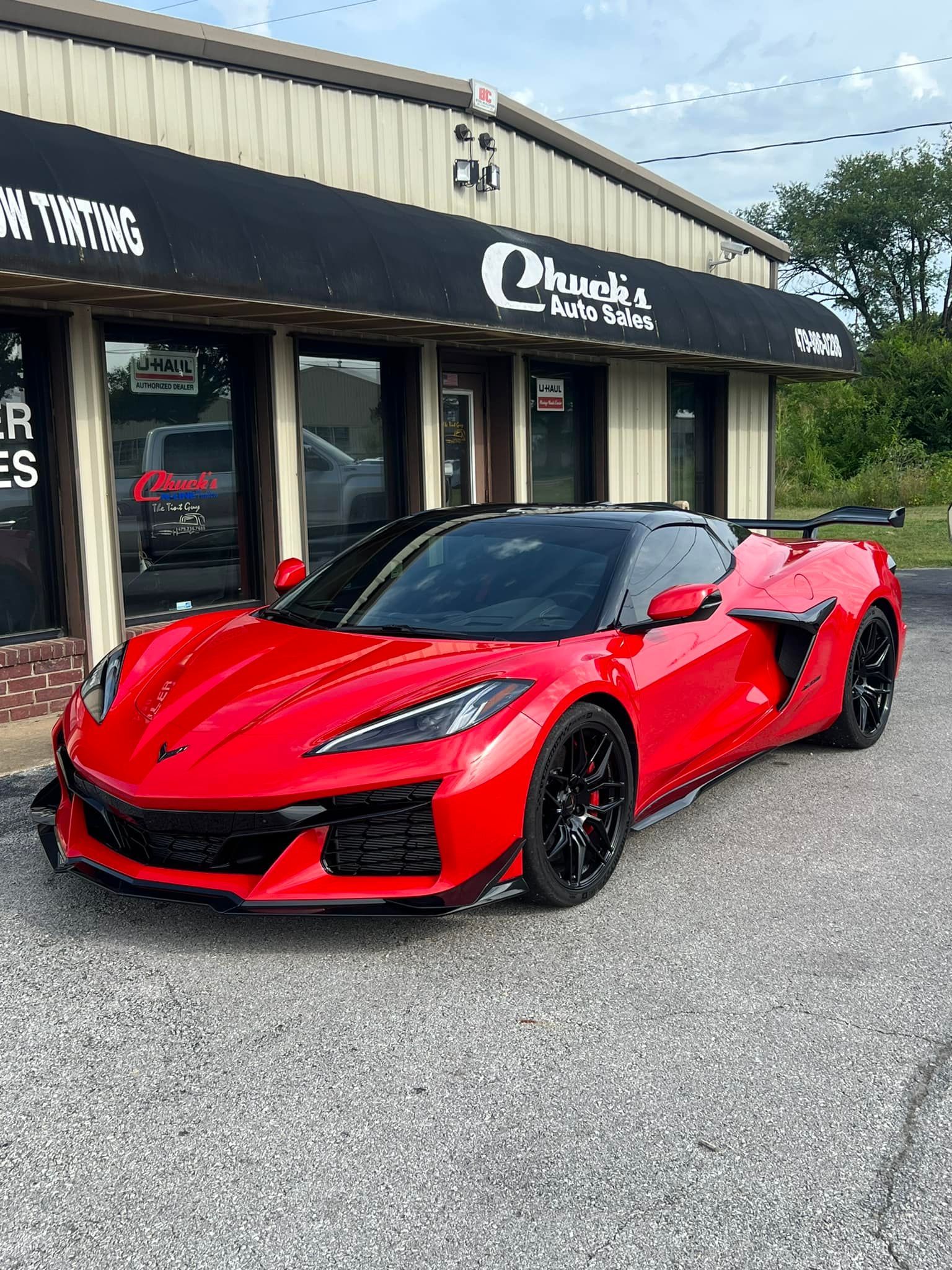 Red Chevrolet Corvette sports car parked outside a shop with black awning.
