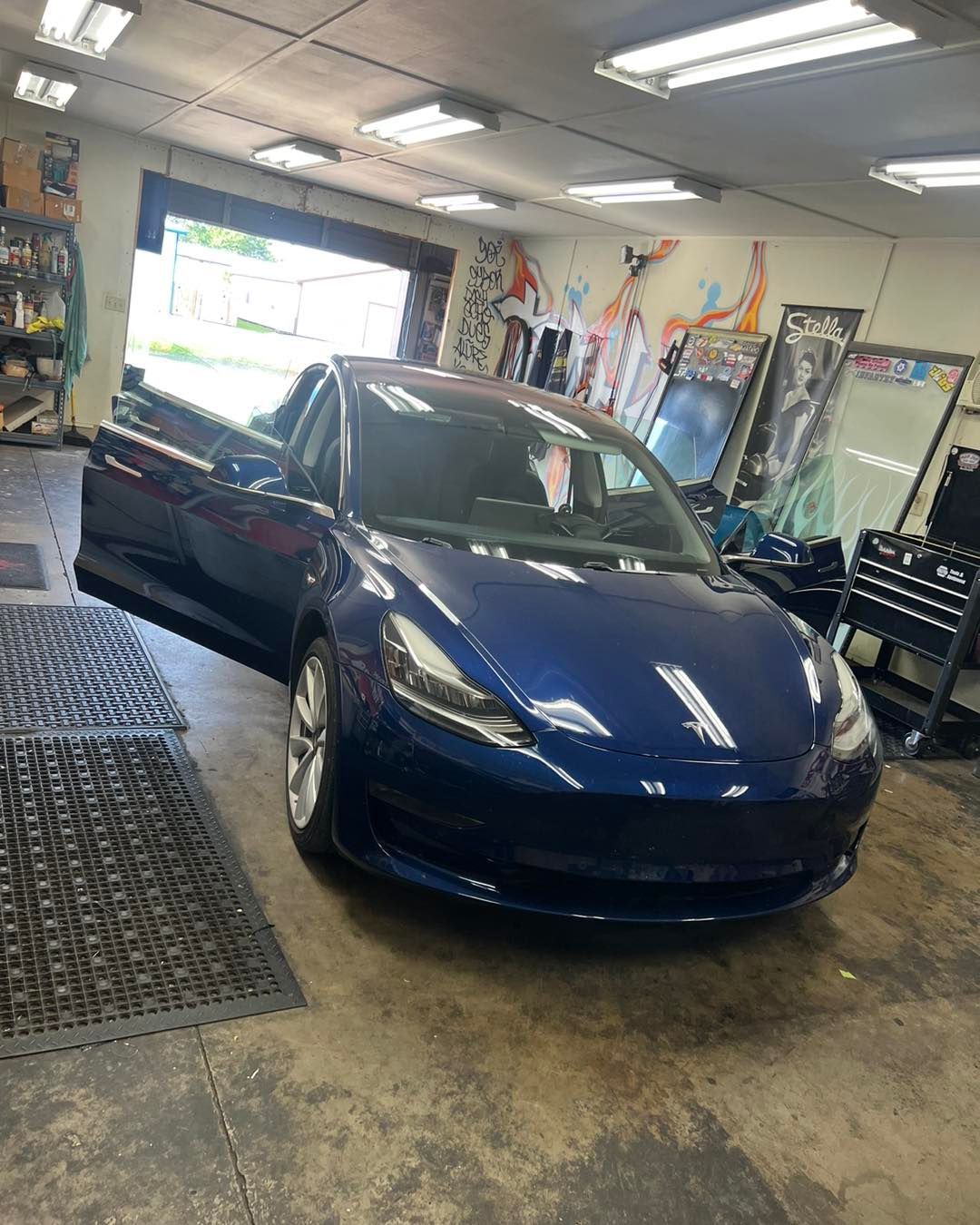 Blue Tesla car with door open inside a garage.