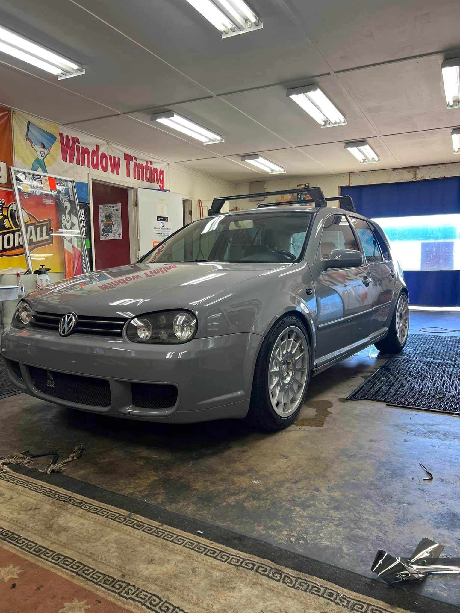 Gray Volkswagen Golf parked inside a garage, possibly for window tinting, with silver wheels.