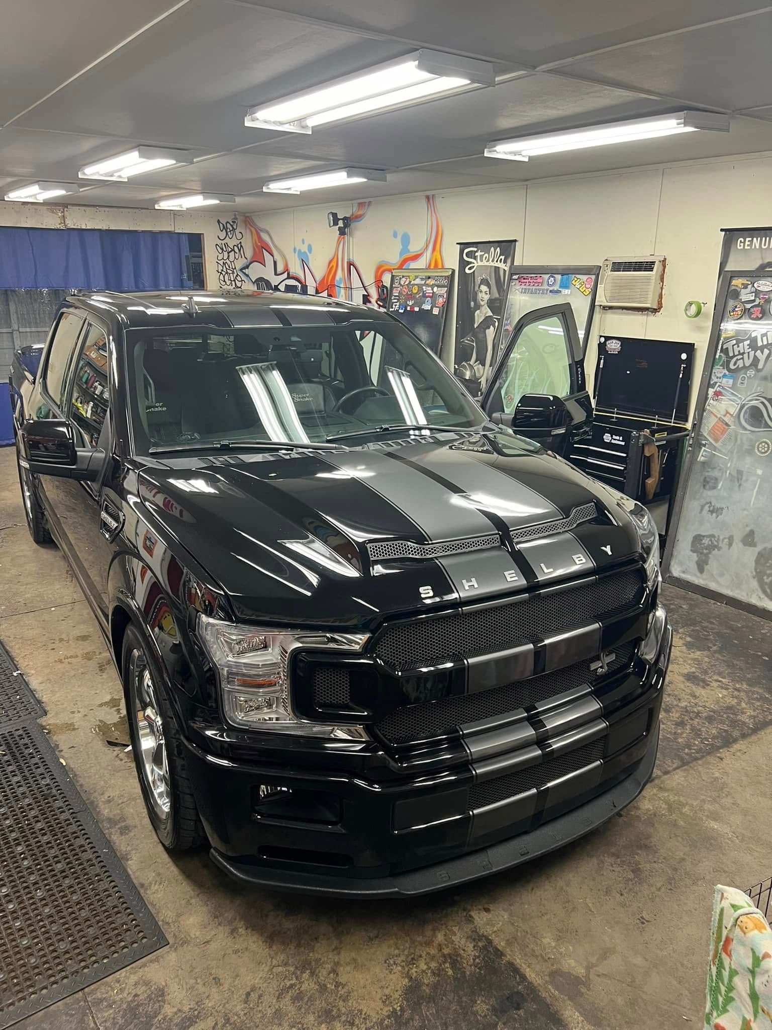 Black Ford truck with racing stripes parked inside a garage.