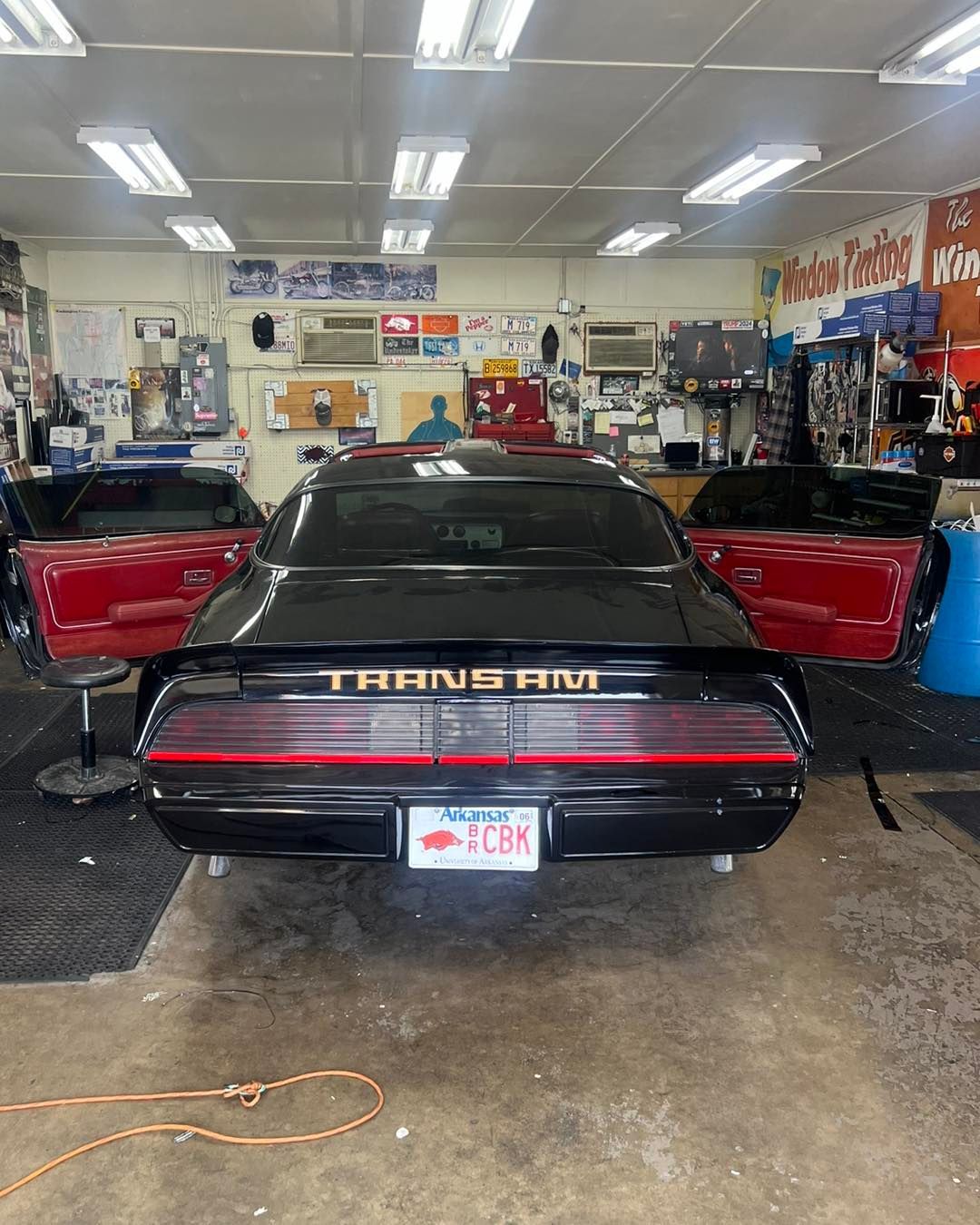 Black Pontiac Trans Am with red interior, doors open, in a garage.