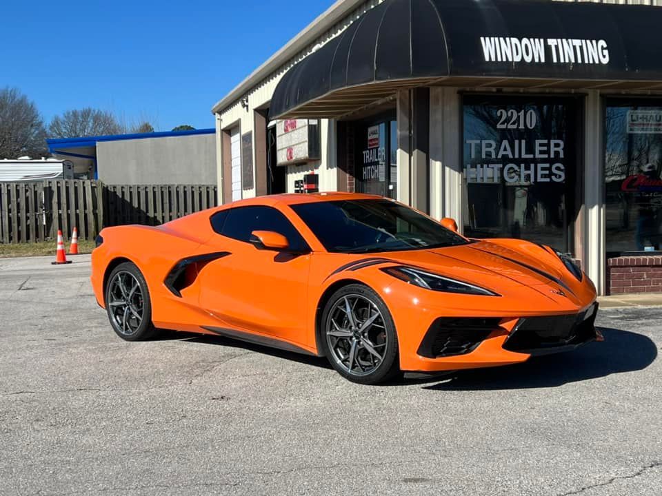 Orange Corvette parked in front of a window tinting business with black awning.