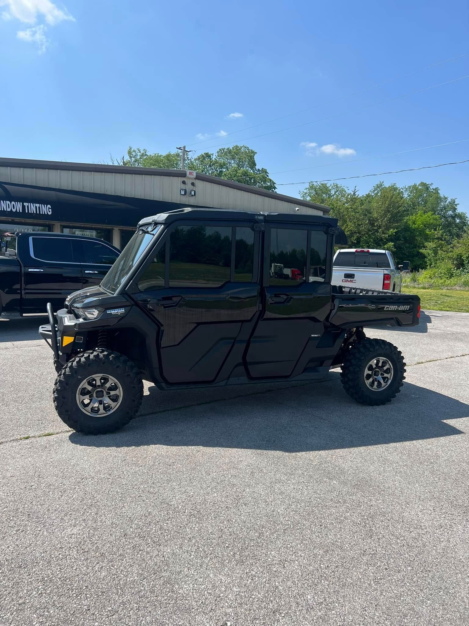 Black Can-Am Defender side-by-side with enclosed cab parked in a gravel lot on a sunny day.