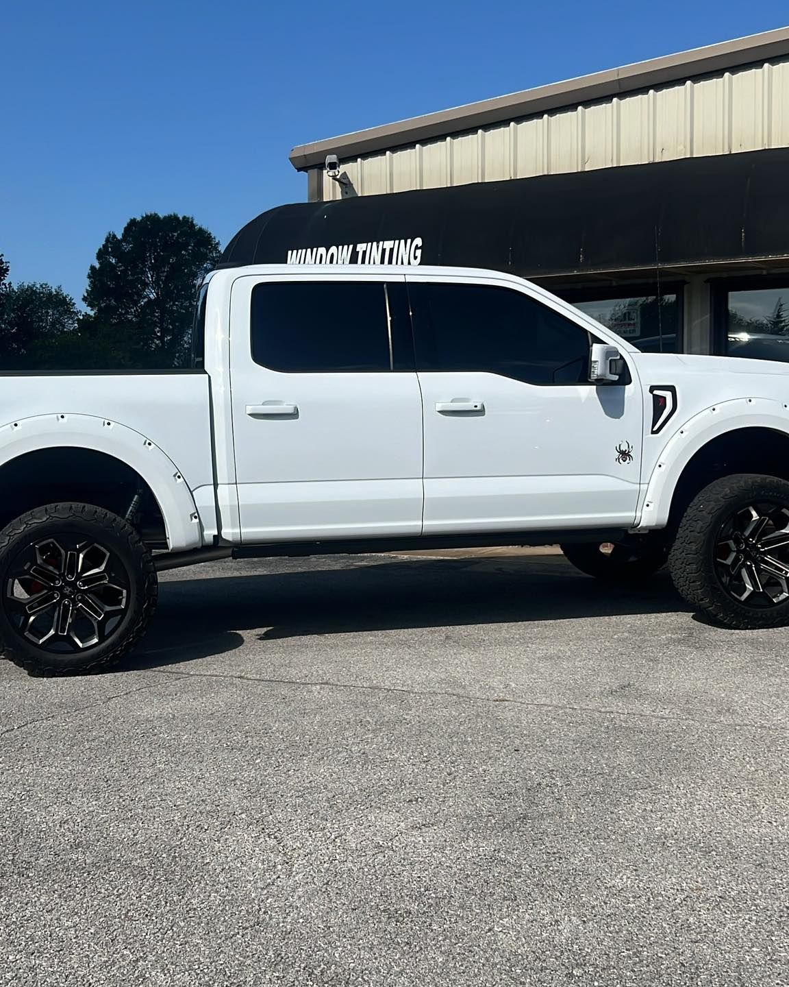 White lifted Ford truck with tinted windows and black wheels parked in front of a building.