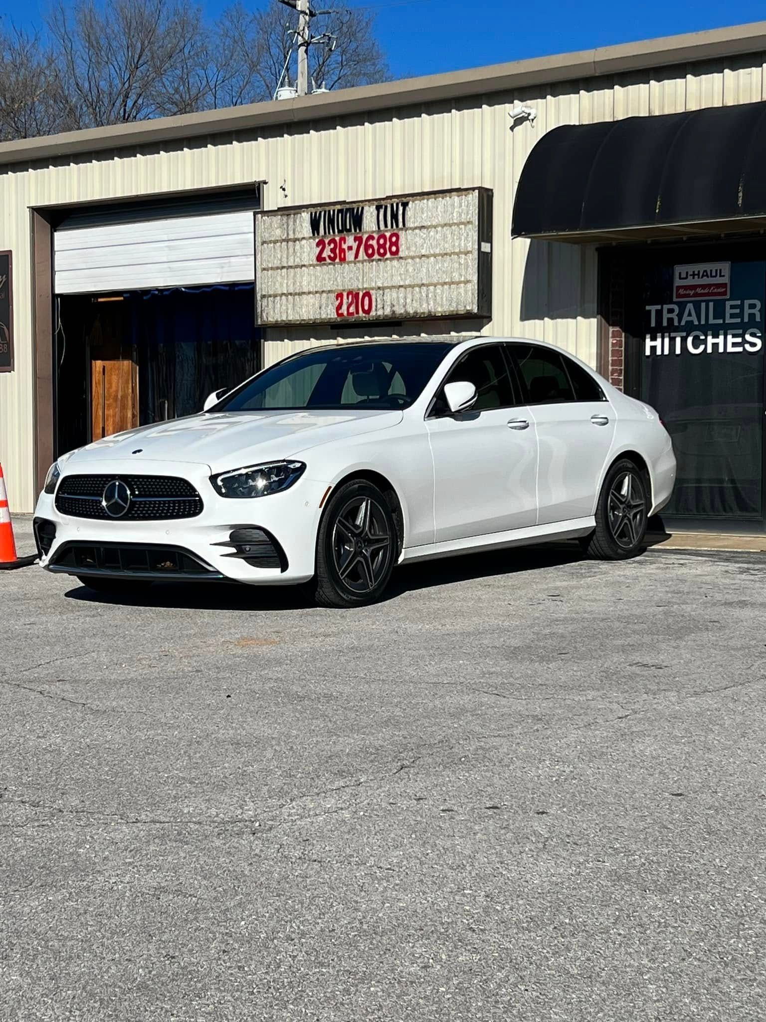 White Mercedes sedan parked outside a building with a trailer hitch sign.