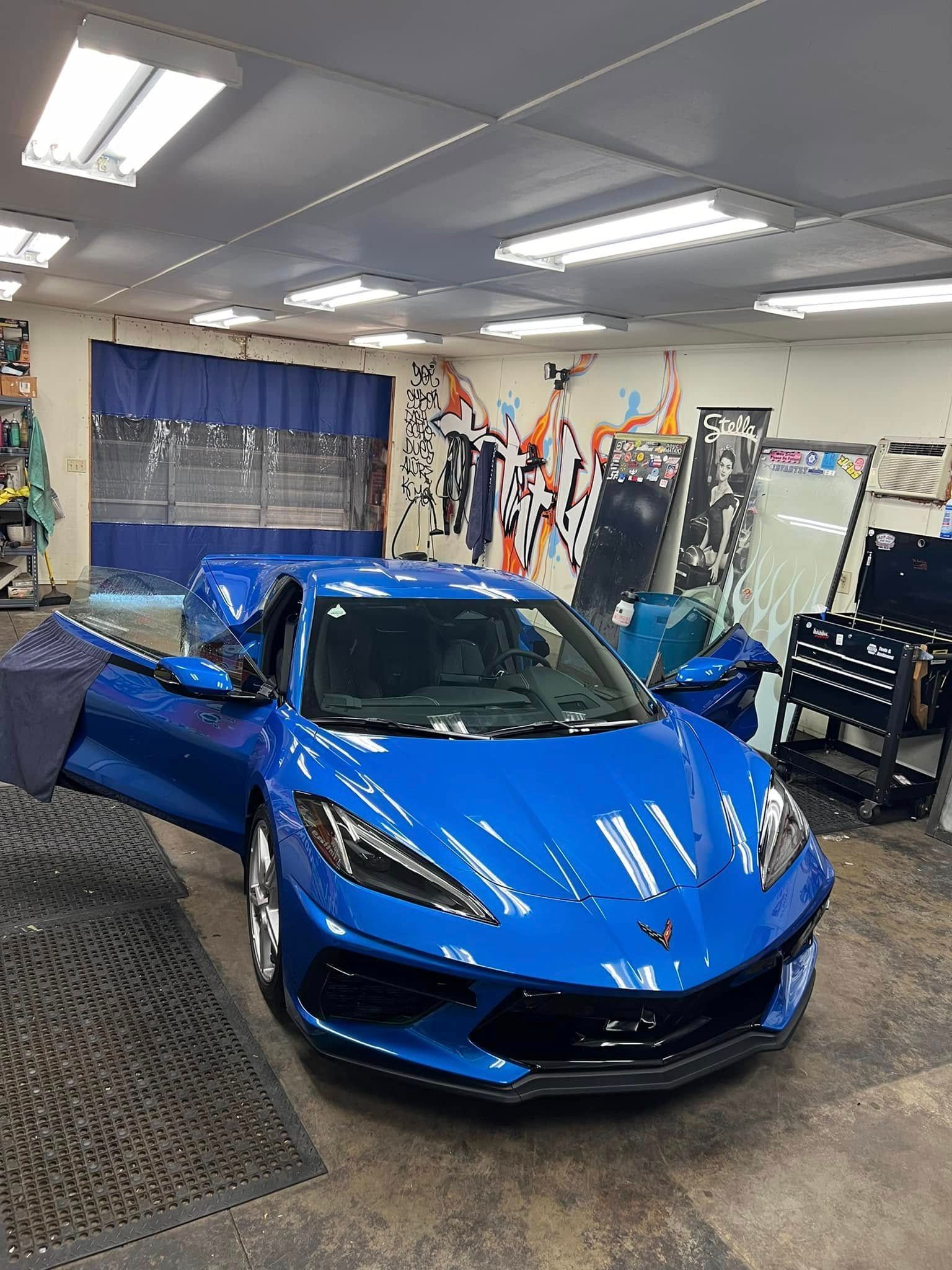 Blue sports car in a workshop, doors open, windows are being tinted.