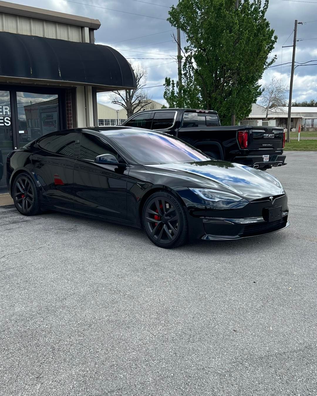 Black Tesla car parked outside a building with tinted windows.