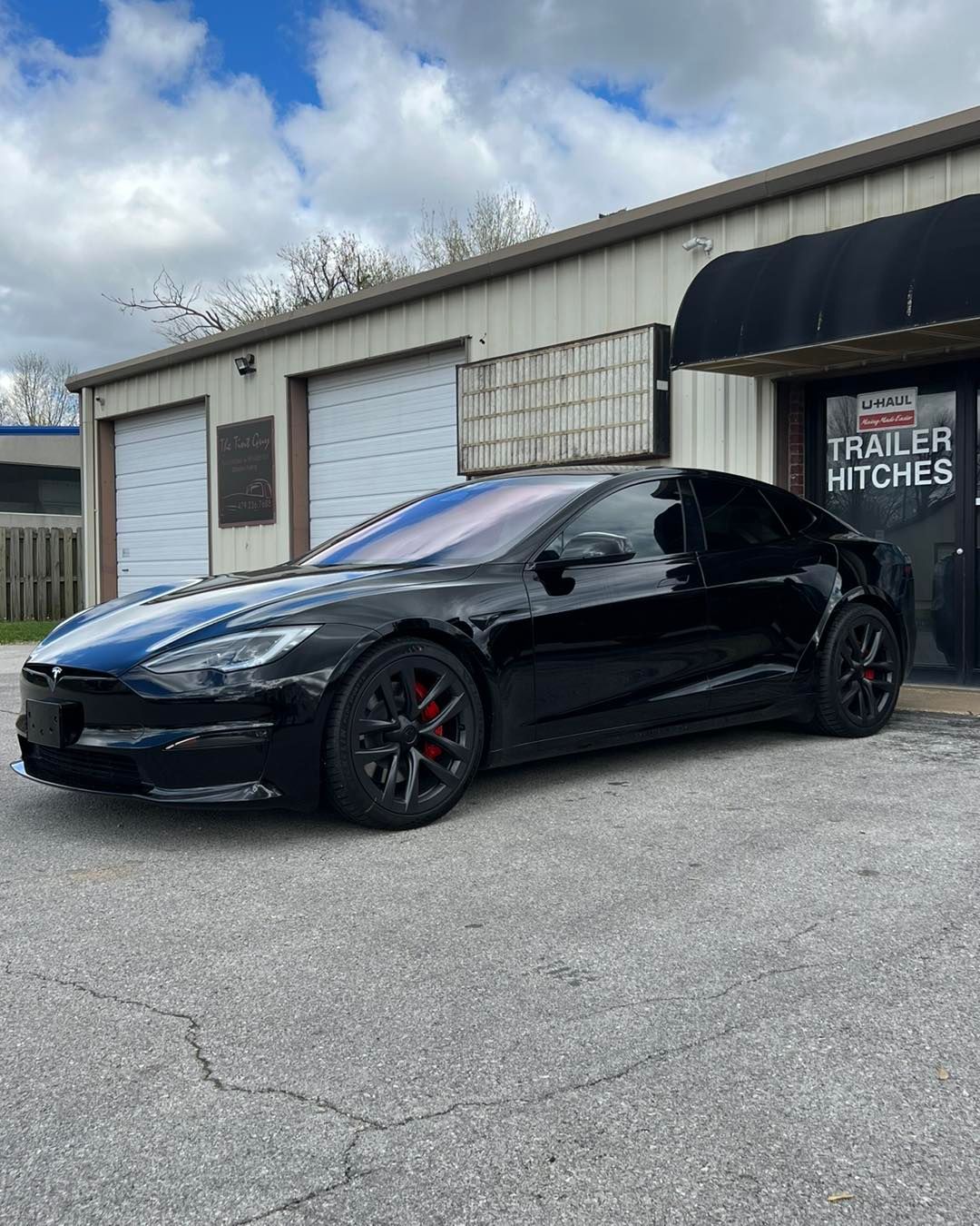 Black Tesla sedan parked in front of a building with a trailer hitch sign.