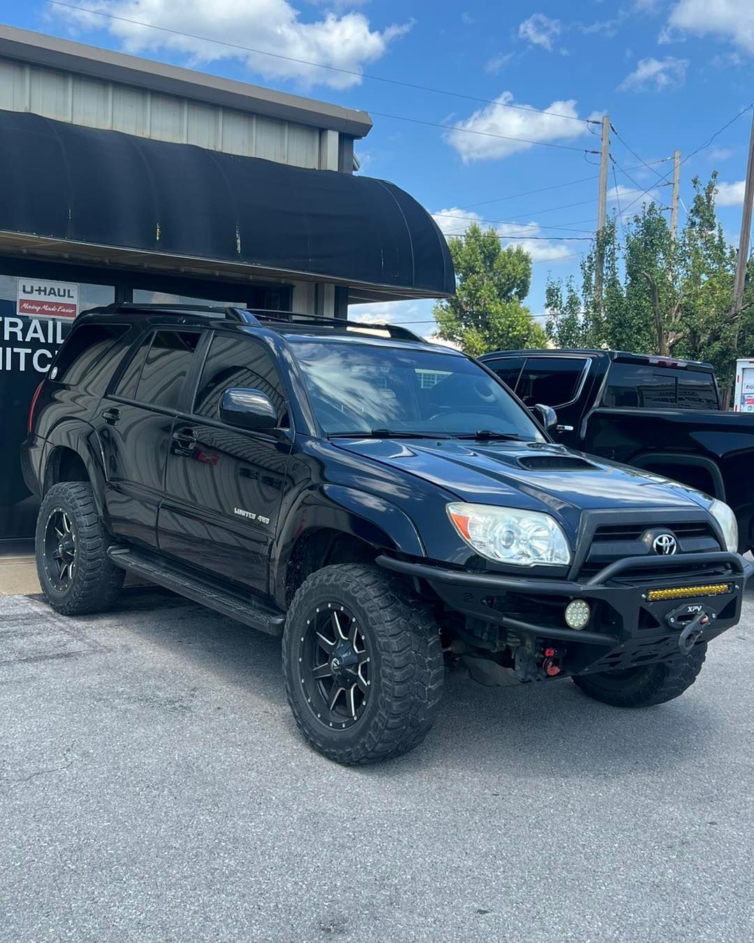 Black Toyota 4Runner SUV, modified with off-road features, parked in front of a building under a blue sky.