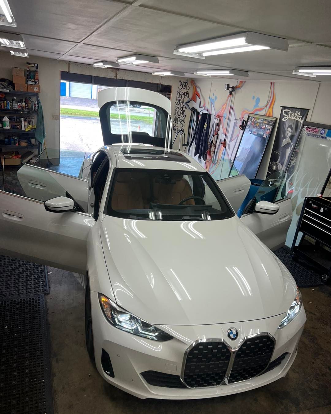 White BMW car with open doors and trunk inside a workshop.