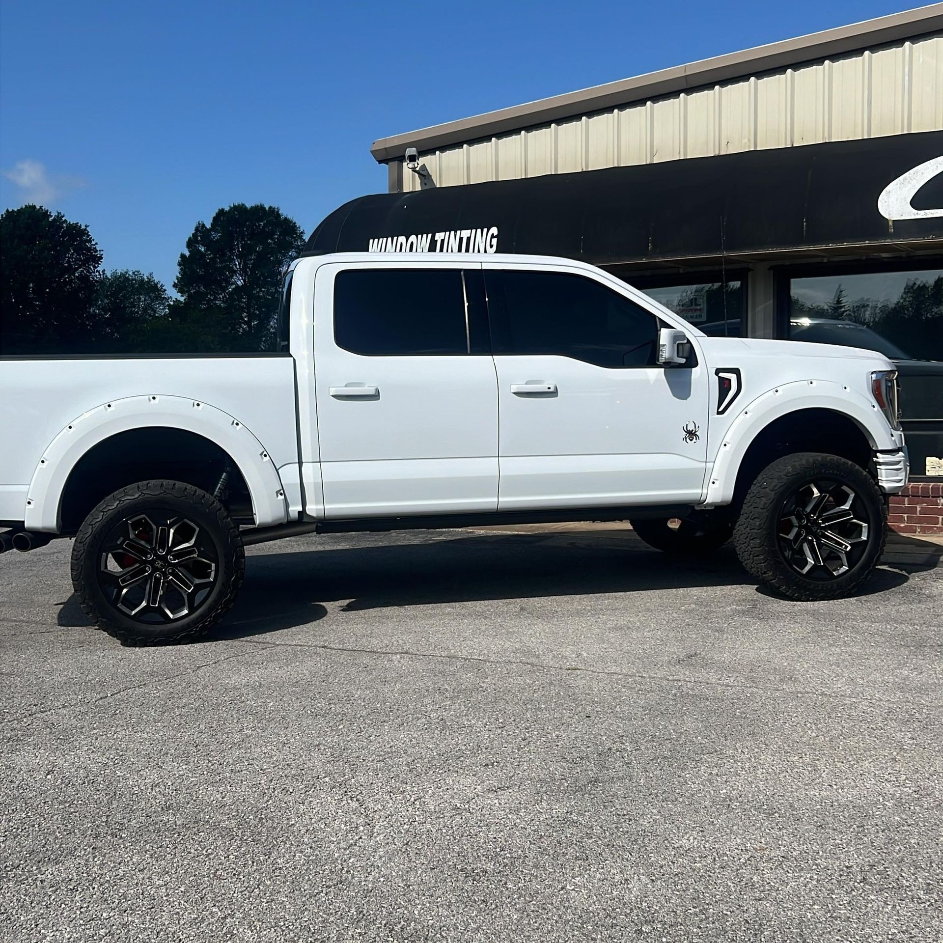 White lifted pickup truck with black wheels parked in front of a building on a sunny day.