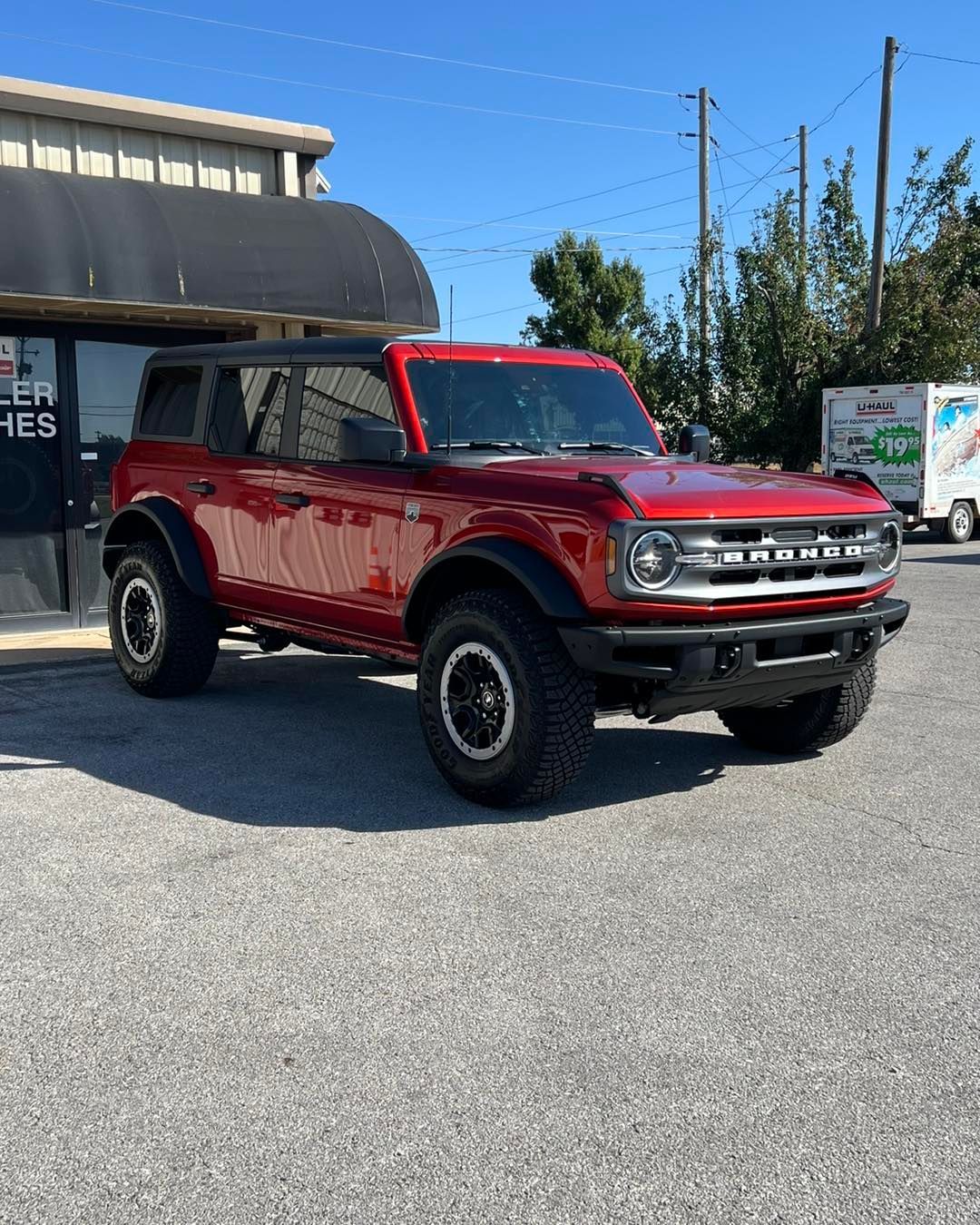 Red Ford Bronco SUV parked in front of a building on a sunny day.