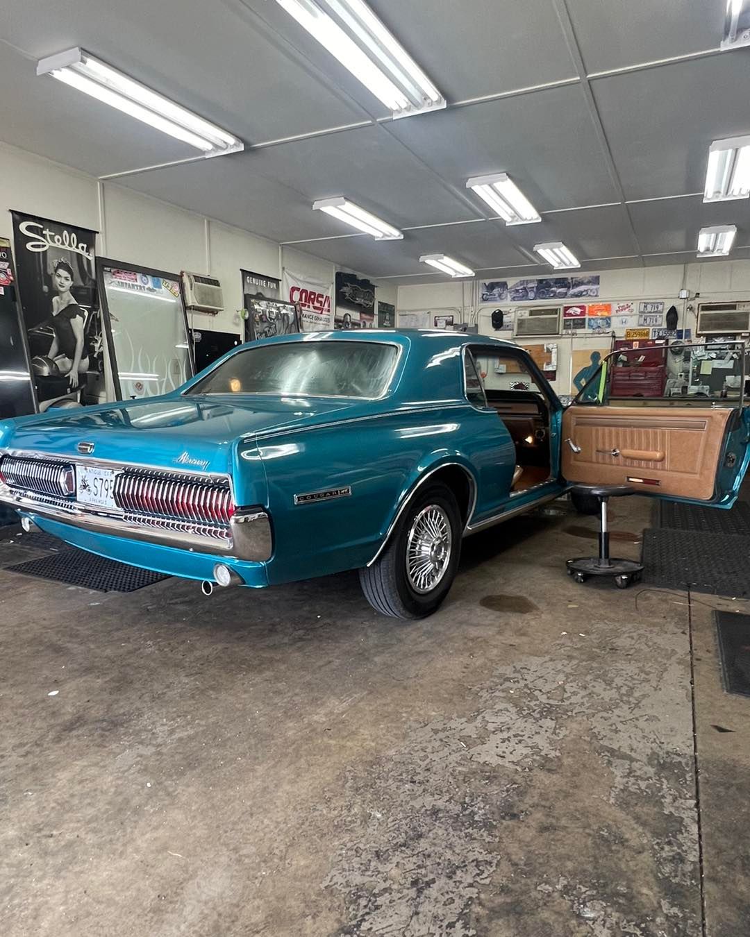 Blue classic Mercury Cougar in a repair shop with door open.