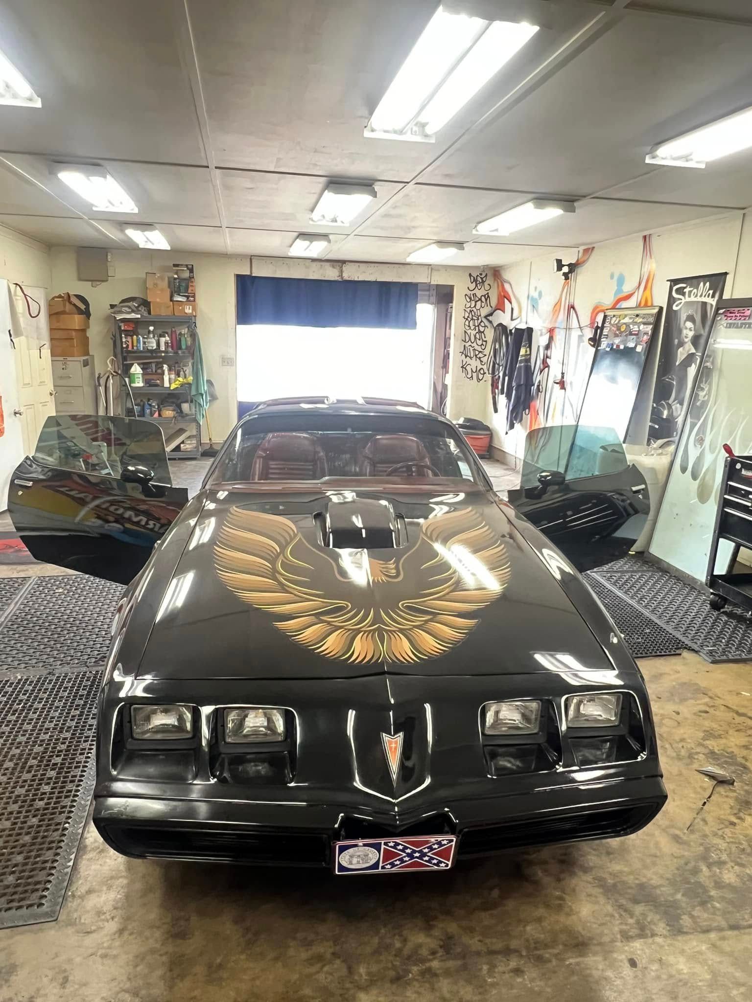 Black Pontiac Trans Am with gold eagle on hood, doors open, inside garage.