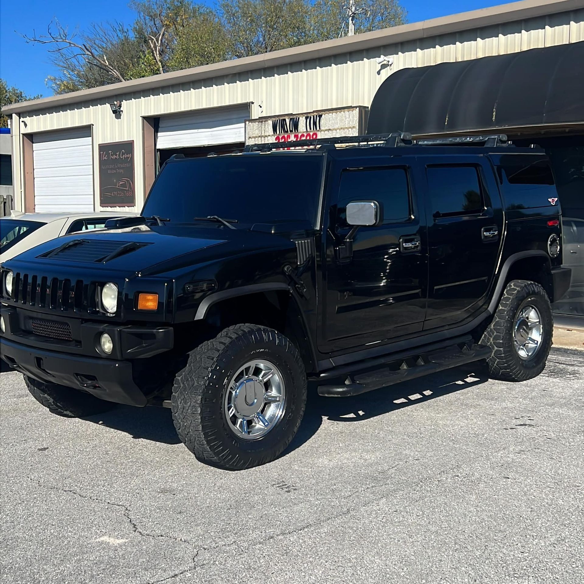 Black Hummer H2 SUV parked outside a building with garage doors. Chrome wheels and tinted windows.