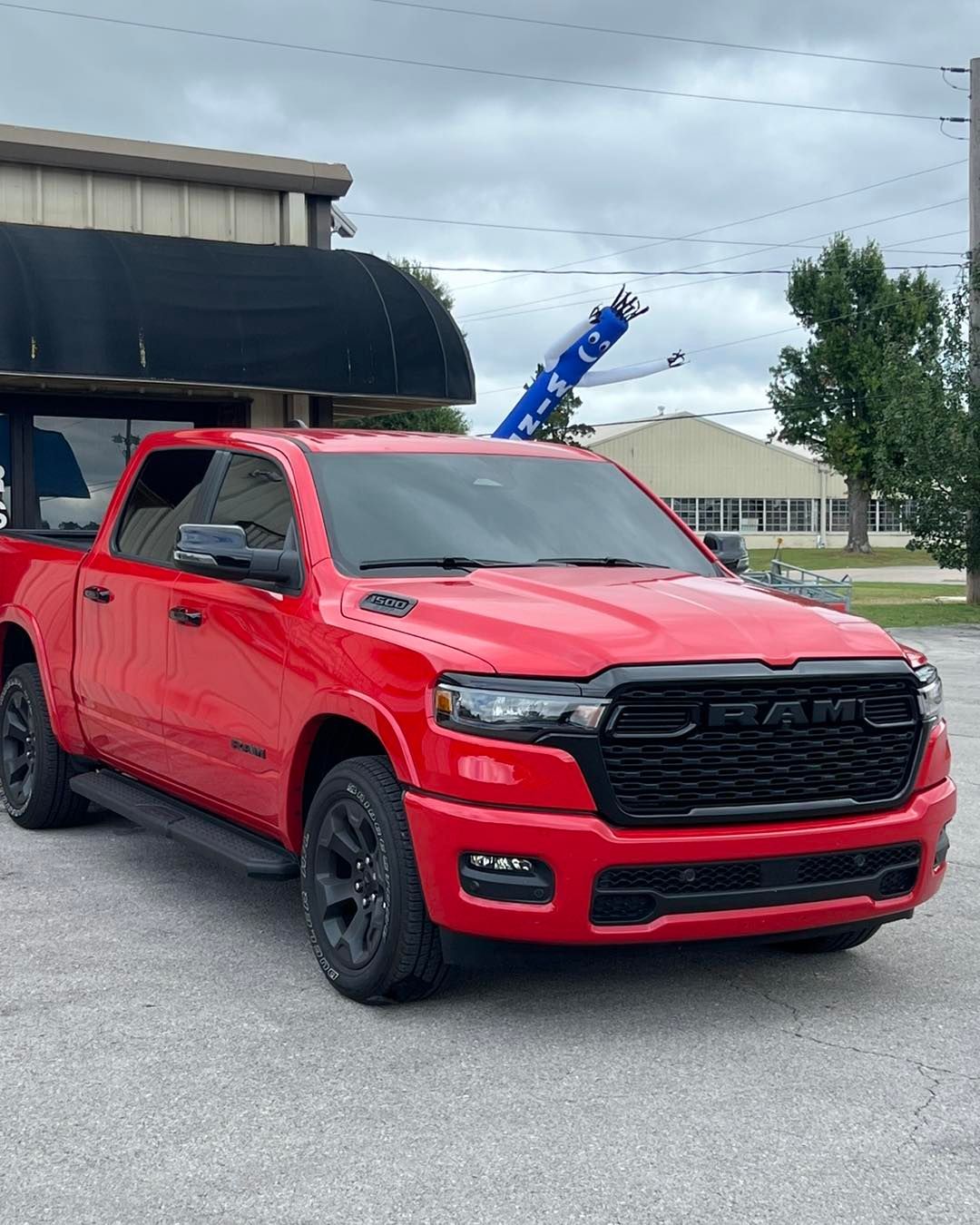 Bright red RAM pickup truck with black trim, parked on a paved lot on an overcast day.
