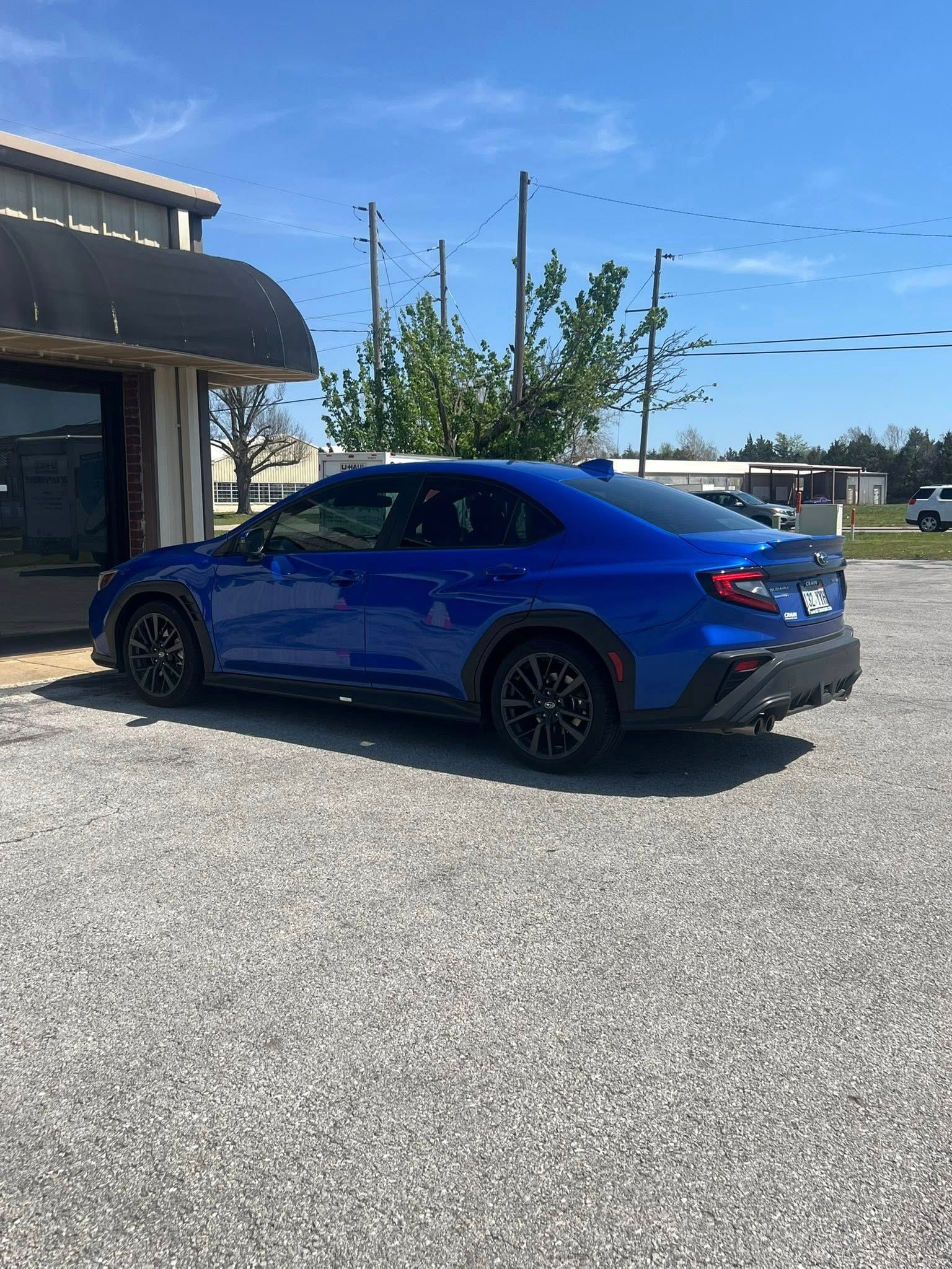 Blue Subaru sedan parked on gravel in front of a building on a sunny day.