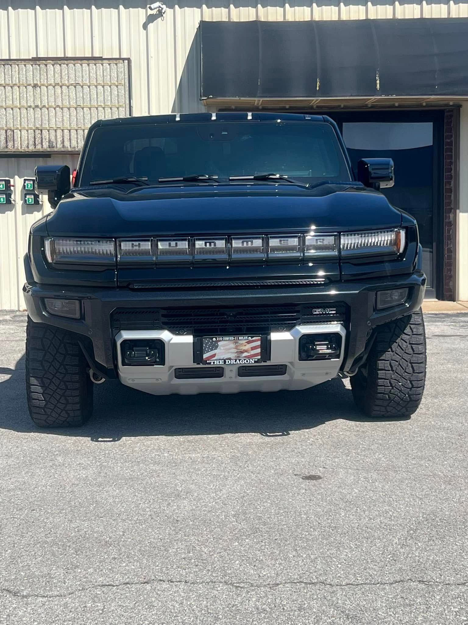 Black Hummer EV SUV parked in front of a building with a silver front bumper and an American flag license plate.