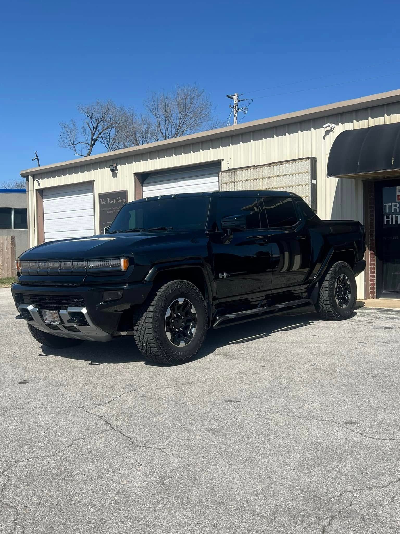 Black Hummer truck parked in front of a building on a sunny day.